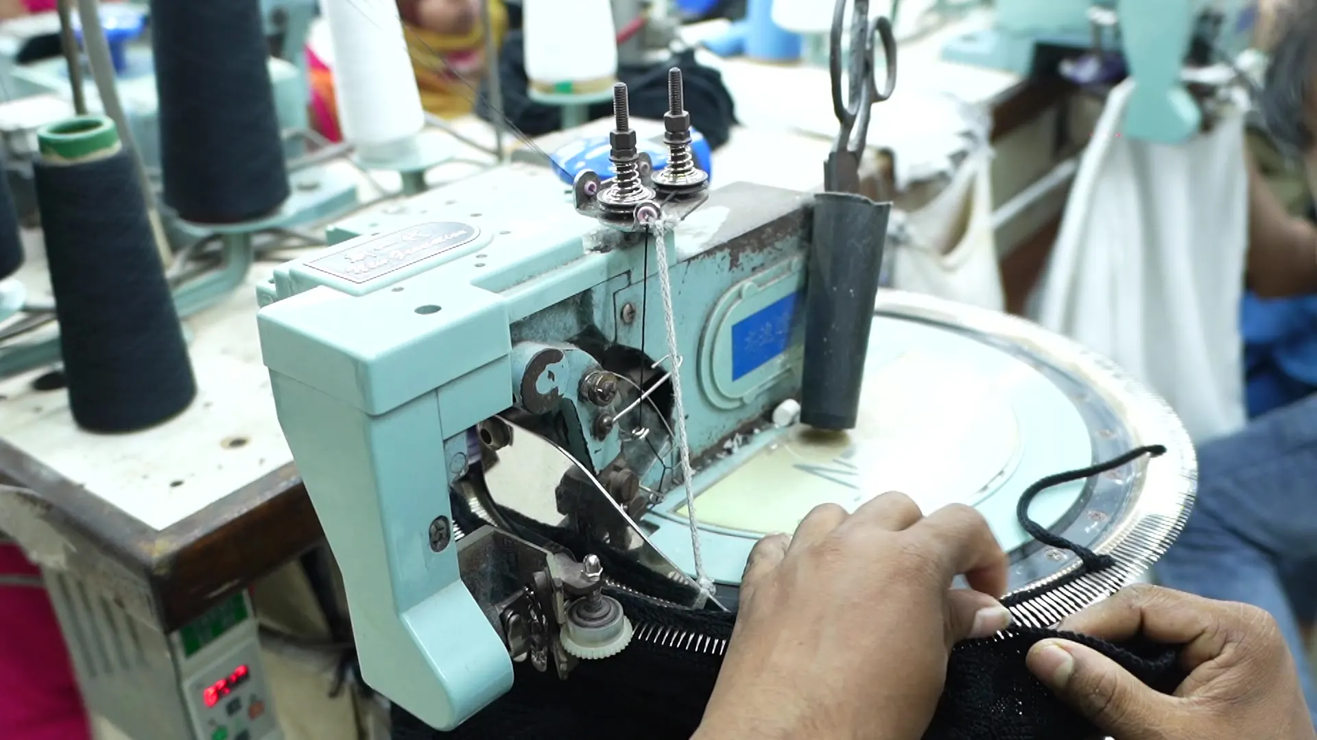 A garment worker guiding knit fabric through an industrial sewing machine