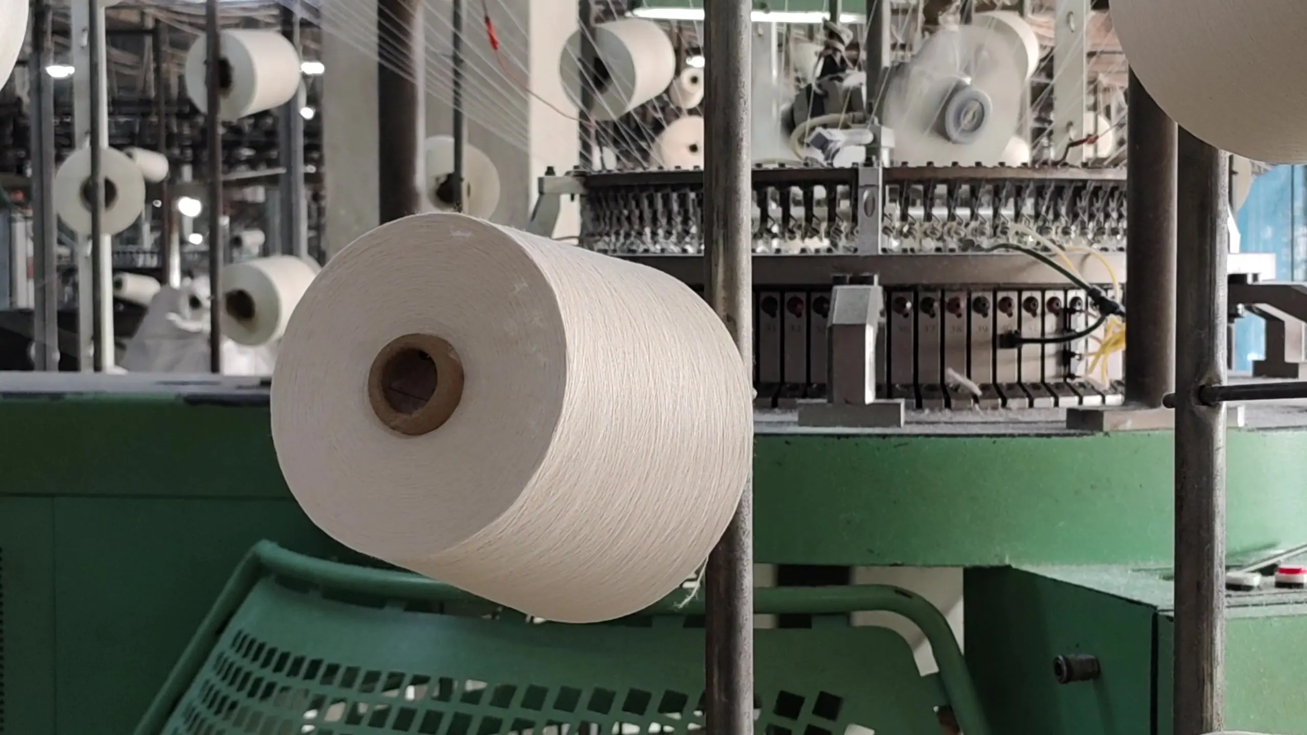 A cone of white cotton yarn feeding a knitting machine