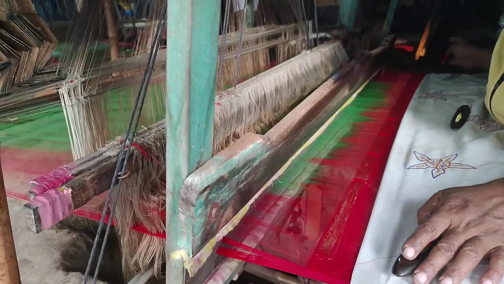 A weaver's hands at a wooden handloom weaving a red and green sari